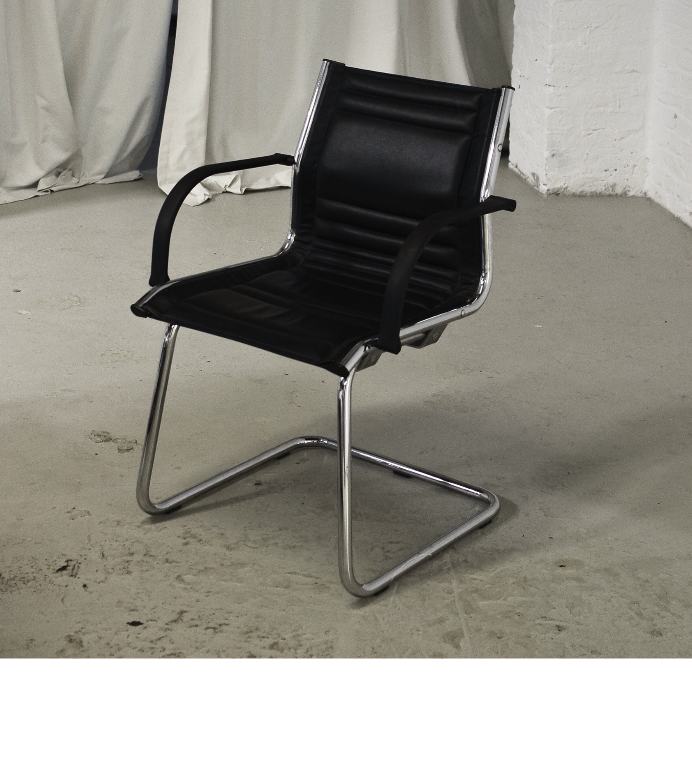 A black office chair in an empty room with white curtains