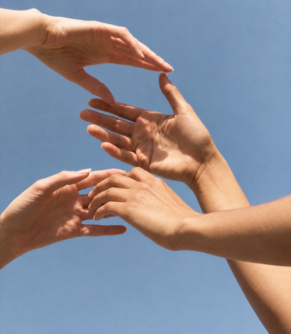 Hands reaching towards each other against a blue sky
