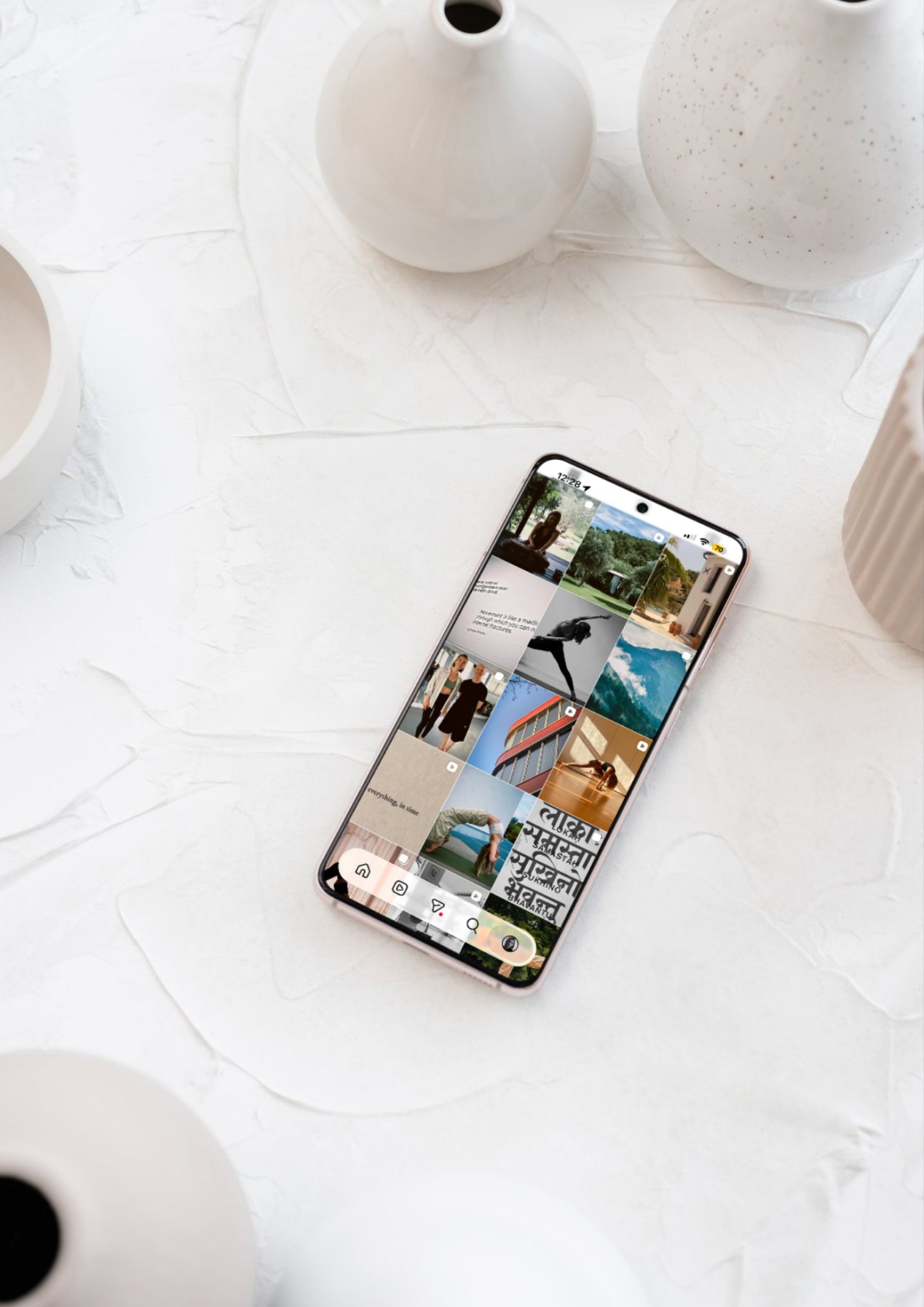 A smartphone showing an Instagram feed on a white textured table with ceramic vases, seen from above