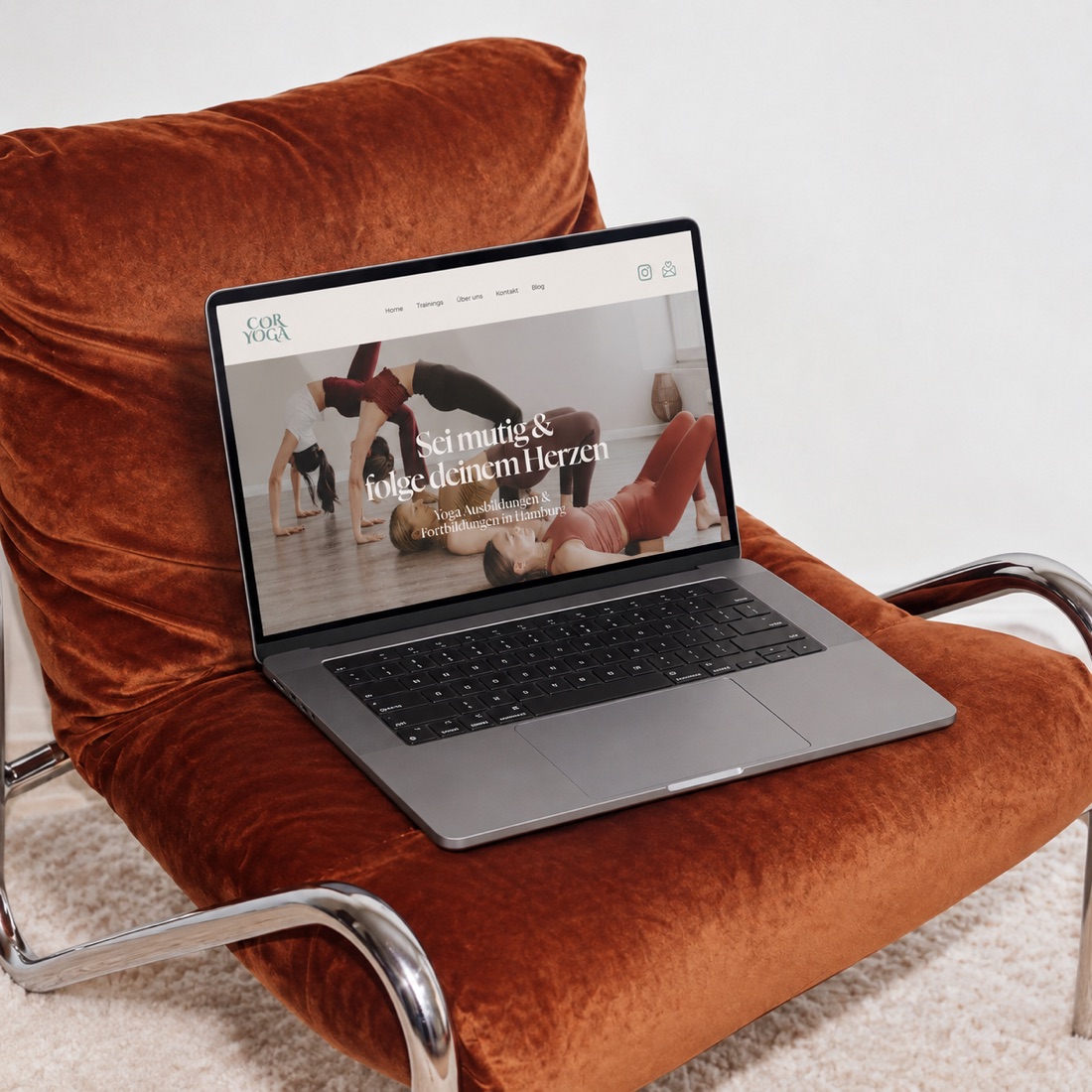 A laptop showing the Coryoga website on an orange velvet armchair